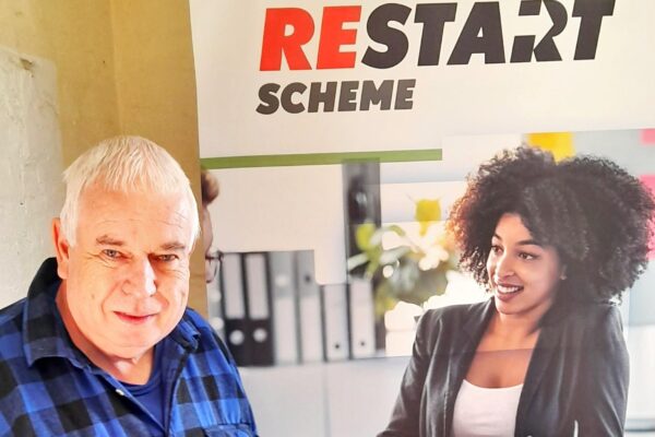 Restart customer, Keith smiling in front of a branded banner